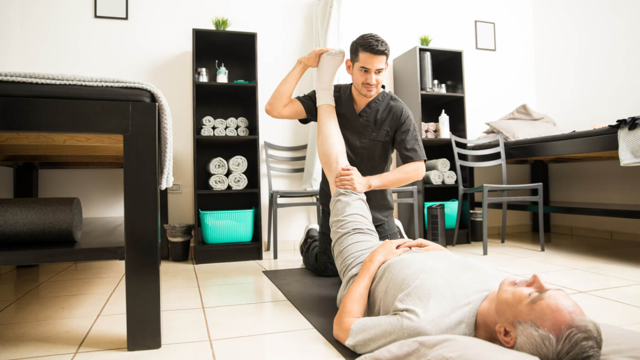 physiotherapy-doctor-assisting-elderly-patient-with-leg-exercise-clinic (1) (1) physiotherapy-doctor-assisting-elderly-patient-with-leg-exercise-clinic (1) (1)
